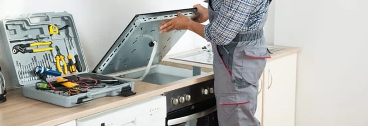 Cooktop repair technician lifting a built-in stovetop for service in Staten Island, NY