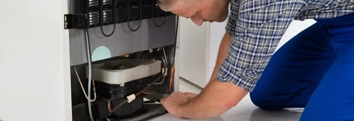 Refrigerator repair technician servicing the compressor and condenser area in Staten Island, NY