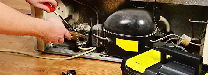 Refrigerator repair technician fixing the compressor and wiring in Staten Island, NY